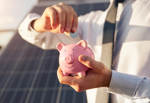 Main d'un homme introduit une pièce de monnaie dans une tirelire en forme de cochon rose